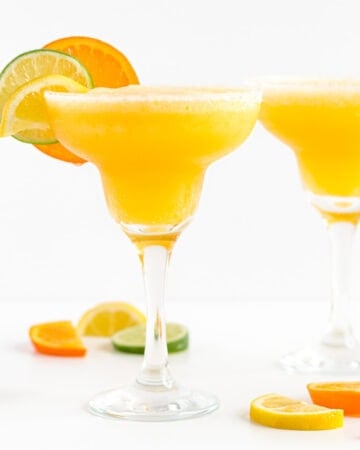 Two margarita glasses filled with frozen citrus margarita and garnished with orange, lemon and lime slices.