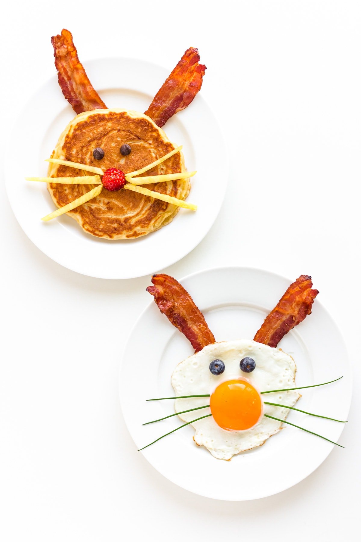 A bunny pancake with bacon ears and a sunny side up fried egg and bacon bunny on separate white plates.