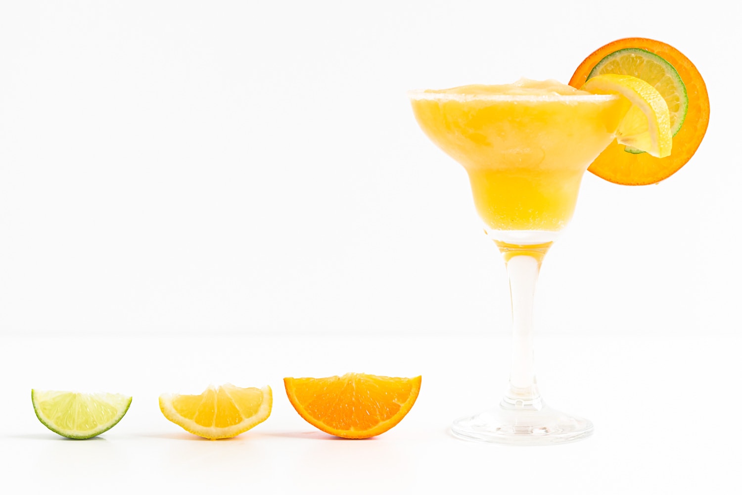 A wedge of lime, lemon and orange next to a glass of frozen citrus margarita.