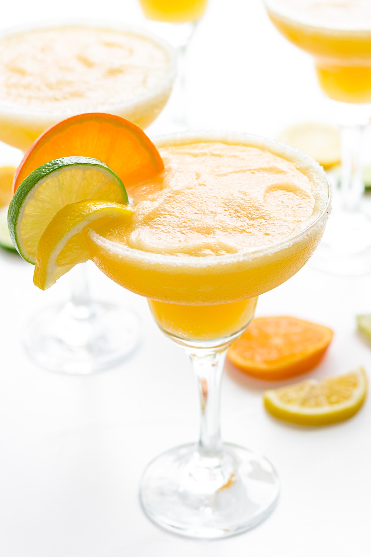 Frozen citrus margaritas garnished with slice of orange, lemon and lime.