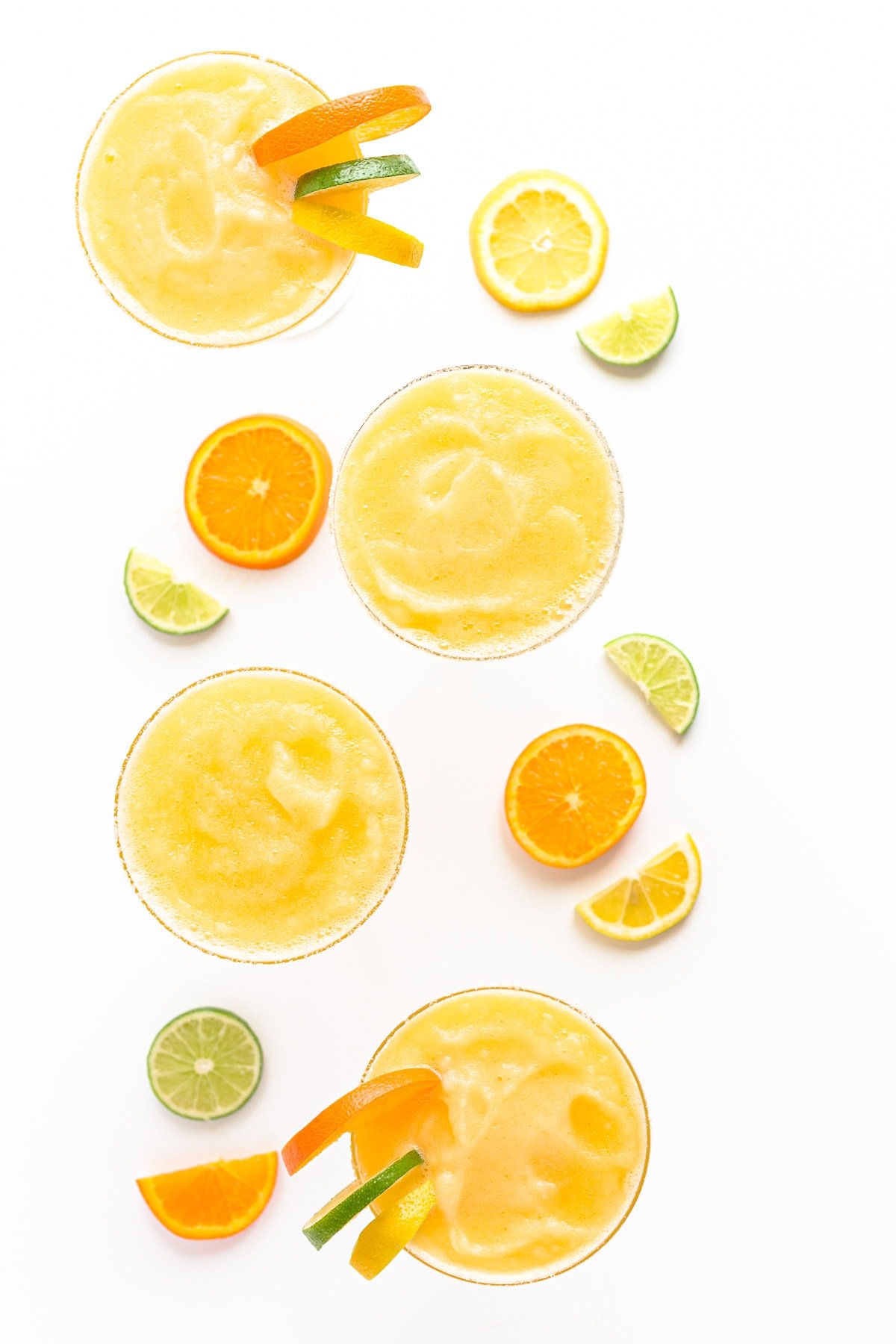 Overhead view of four citrus margaritas garnished with orange, lemon and lime slices.