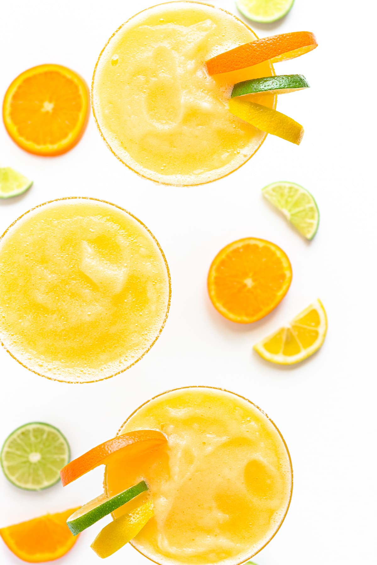 Overhead view of three frozen margaritas garnished with orange, lemon and lime slices.