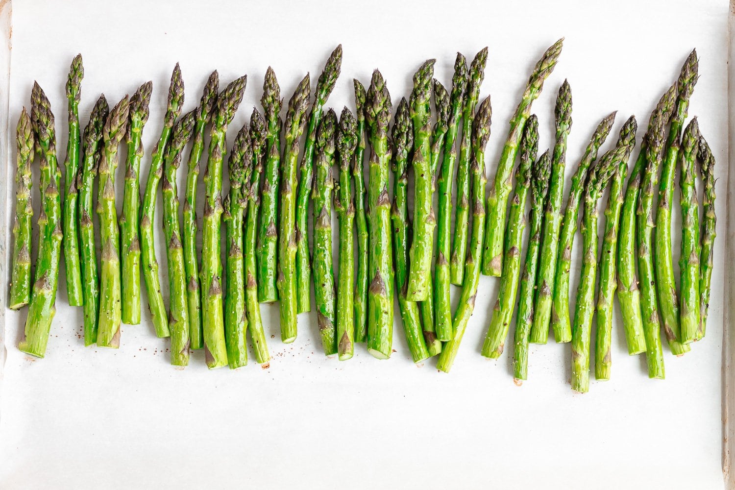 Roasted asparagus on a parchment paper lined baking sheet.