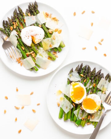 Two plates of roasted asparagus salad, one topped with a poached egg and the other topped with a soft boiled egg.
