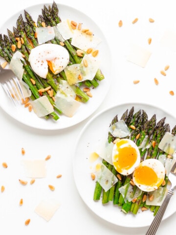 Two plates of roasted asparagus salad, one topped with a poached egg and the other topped with a soft boiled egg.