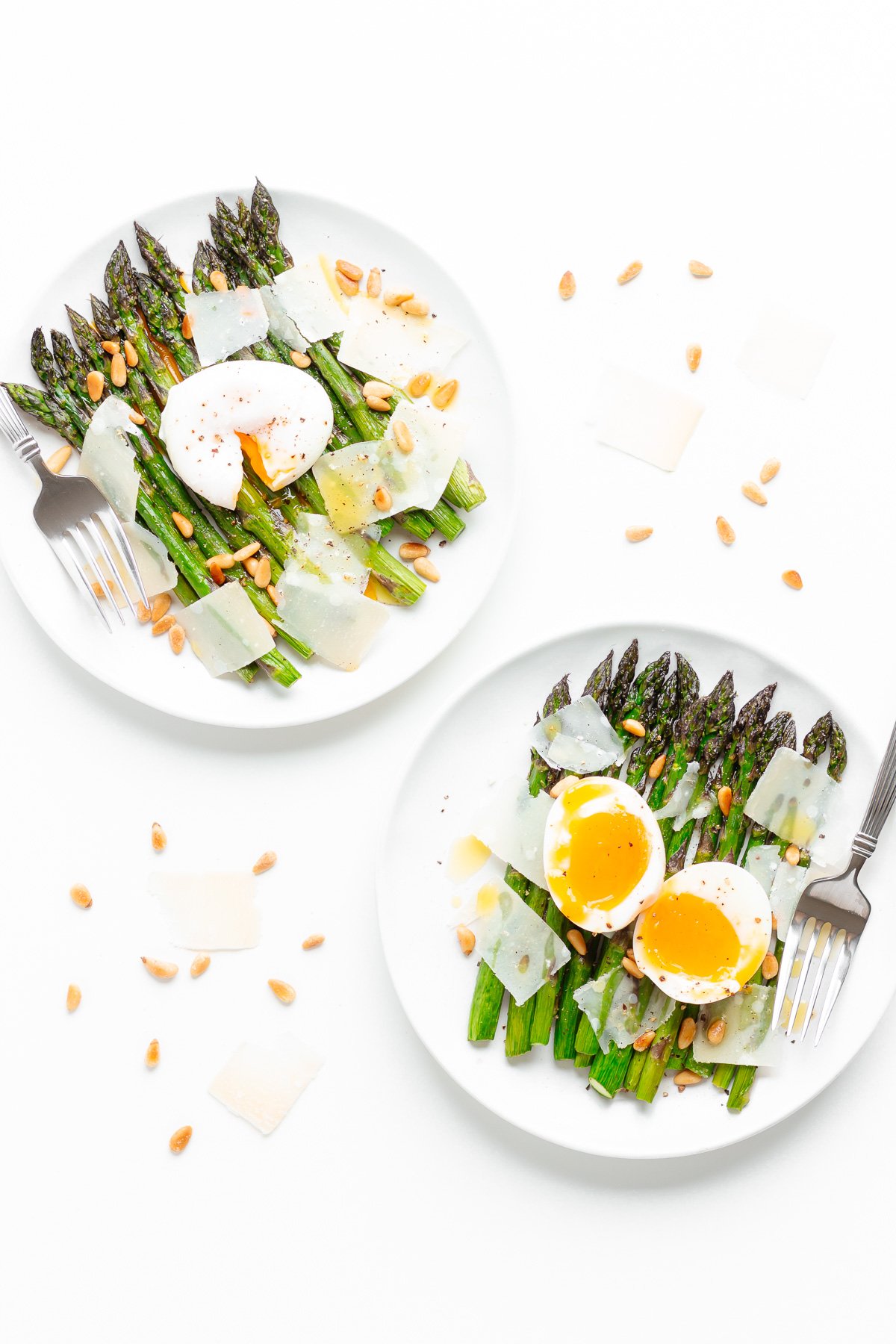 Two plates of roasted asparagus salad with one featuring a poached egg on top and the other a soft boiled egg cut in half.