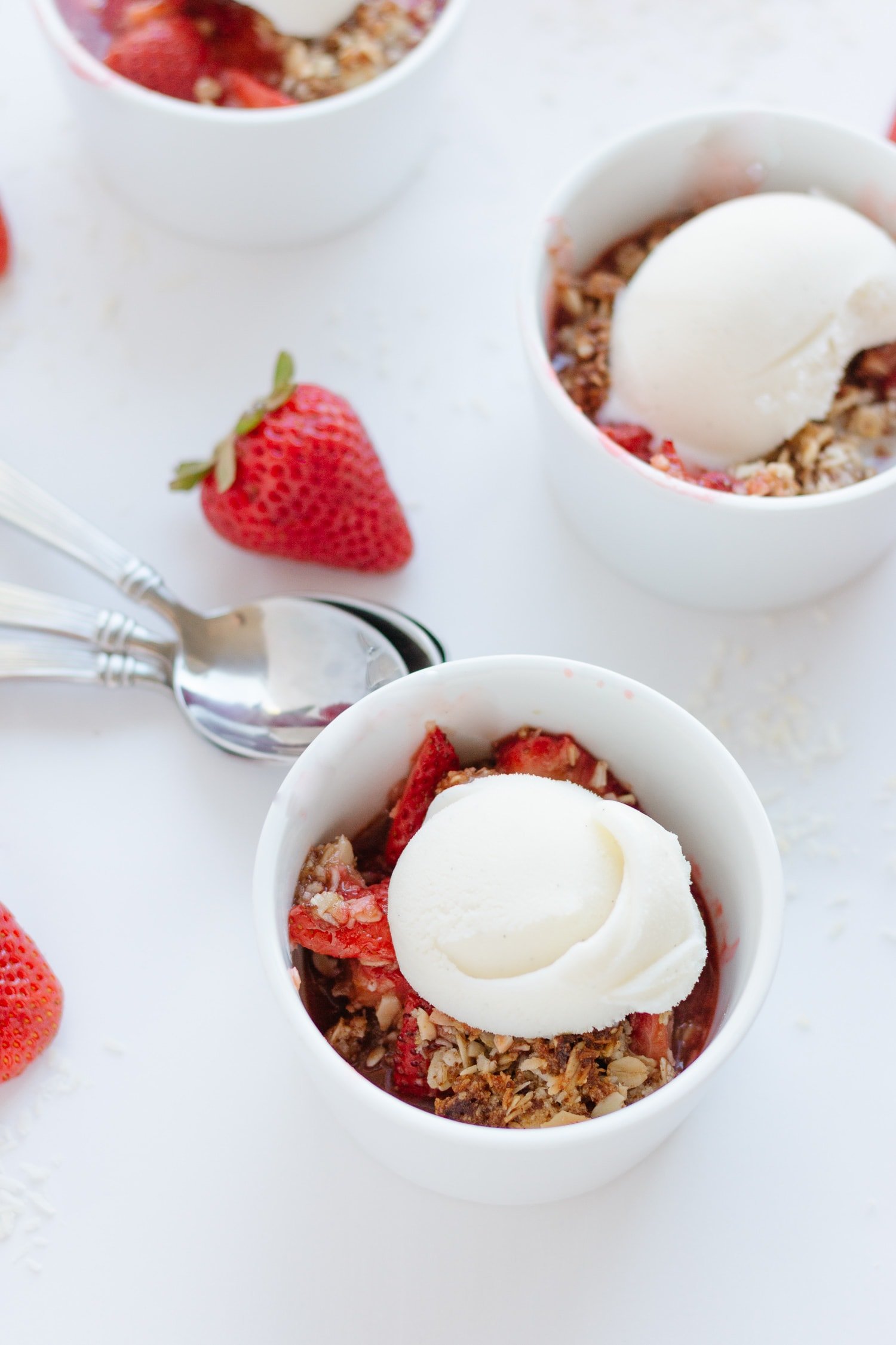 Strawberry Coconut Crisp in three white ramekins topped with a scoop of vanilla ice cream