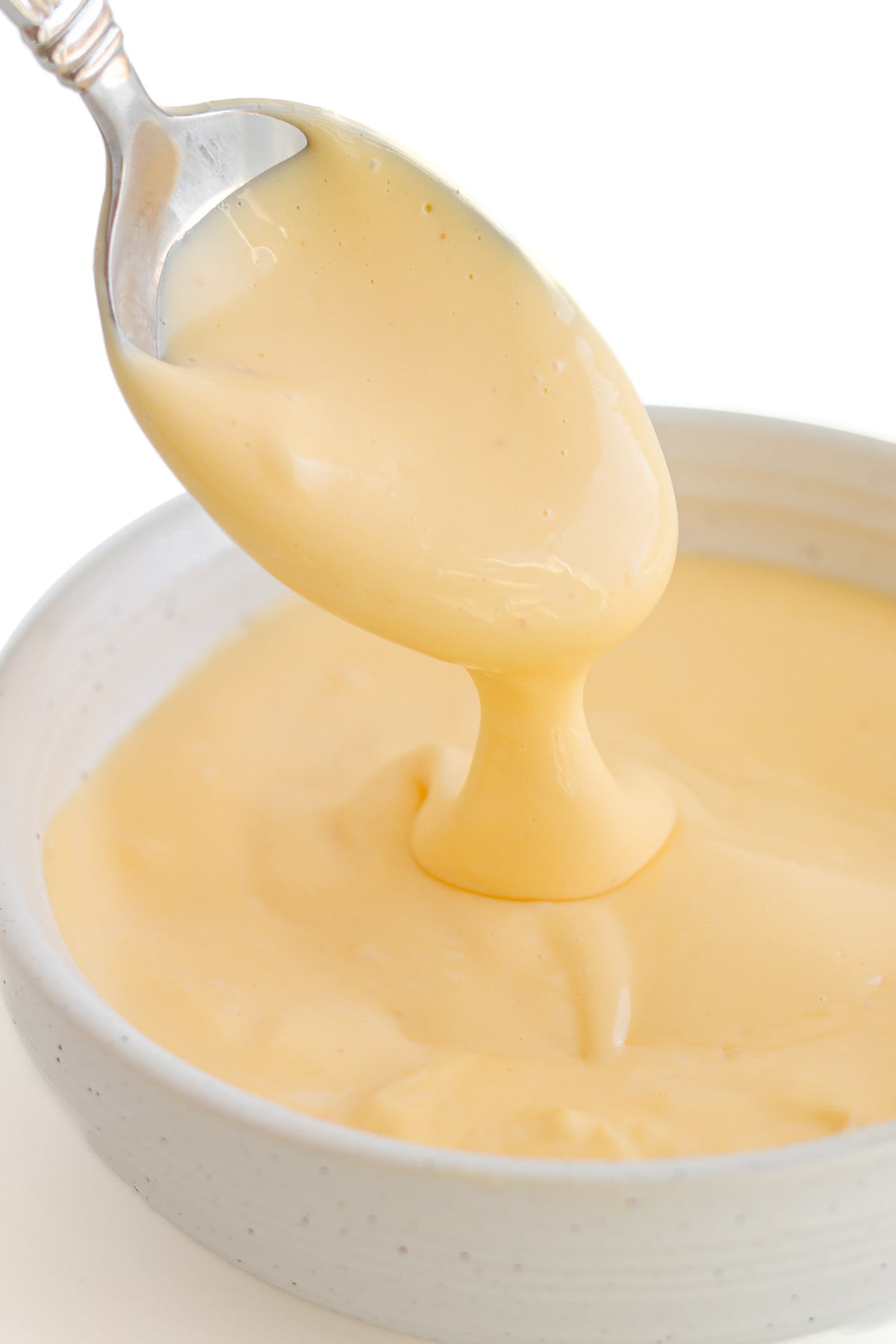 Spoon lifting hollandaise sauce out of a small bowl.