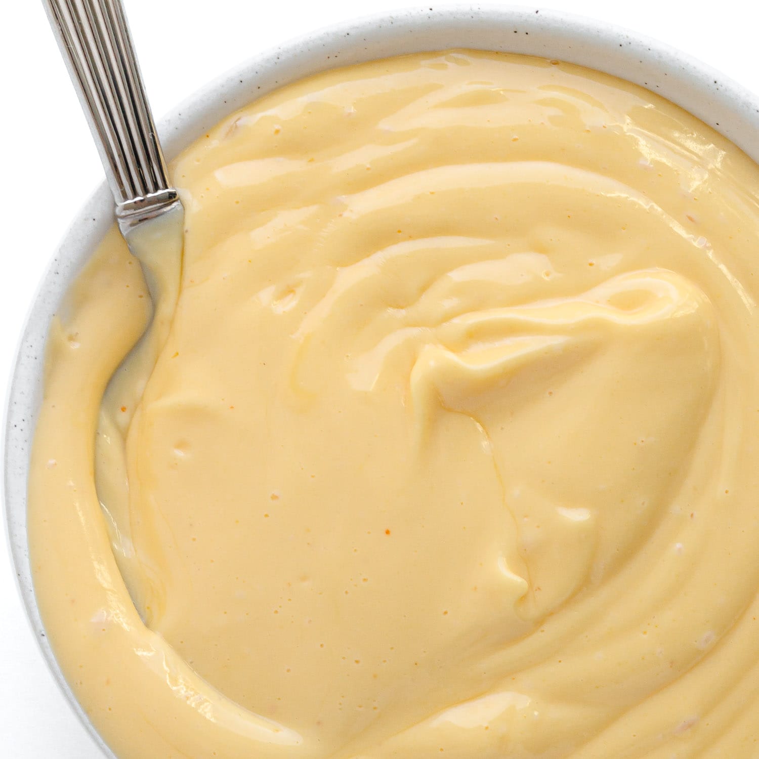 Small white bowl of hollandaise sauce with a spoon.
