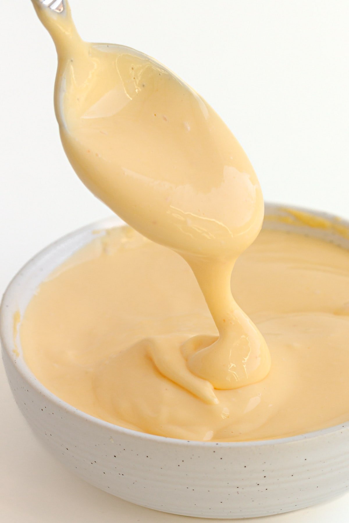Spoonful of hollandaise sauce drizzling into the bowl beneath it.