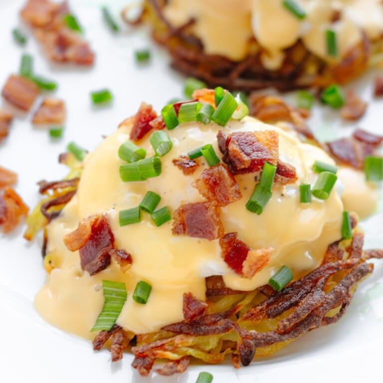 Closeup of eggs Benedict on a potato rosti garnished with chopped bacon and chives.