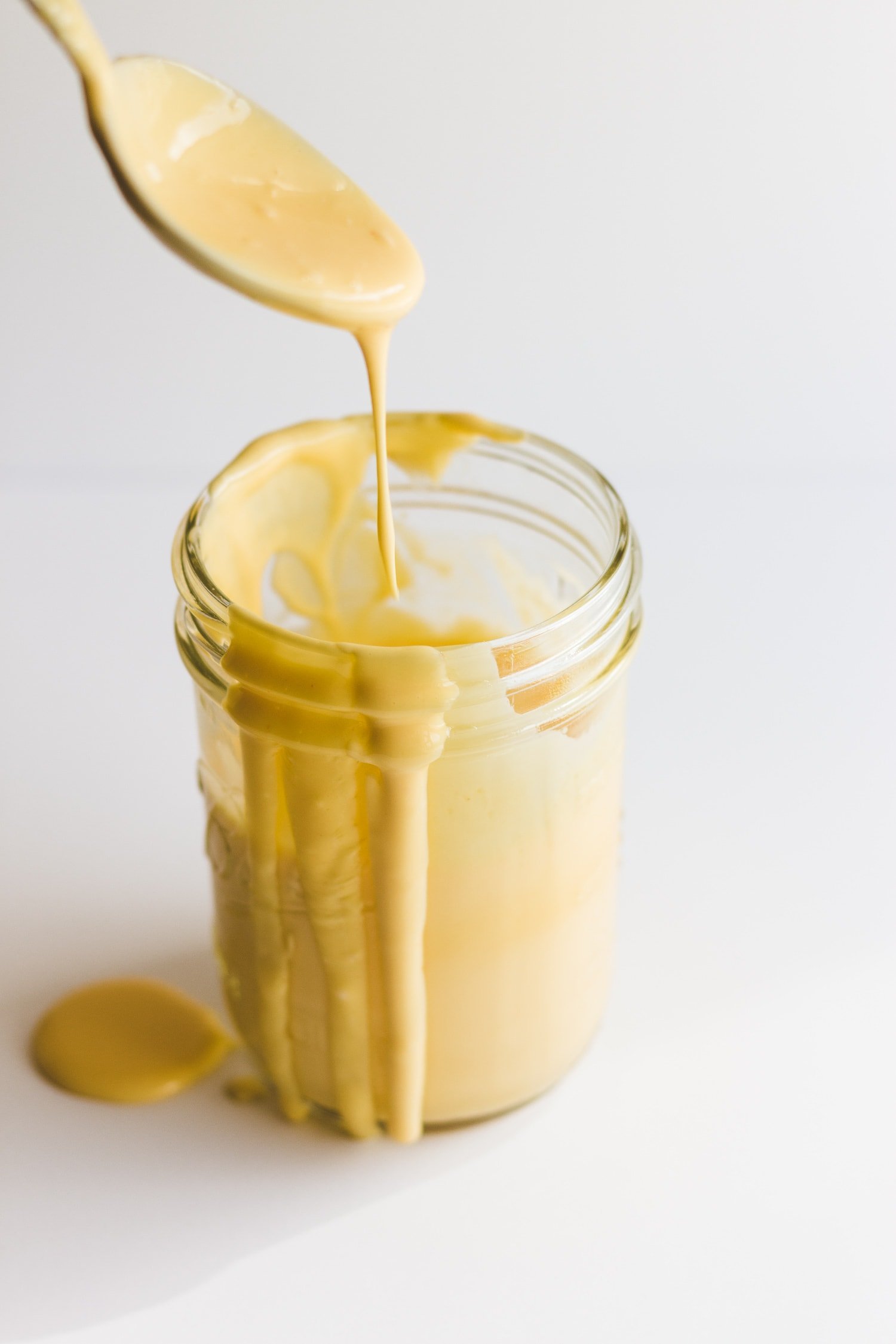 Hollandaise sauce dripping off of a spoon into a mason jar filled with sauce.