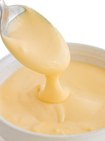 Hollandaise sauce drizzling off a spoon into a small white bowl.