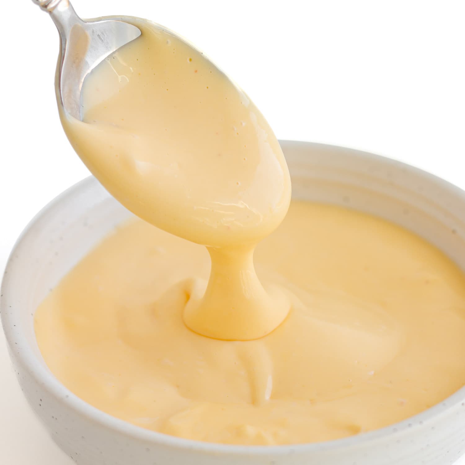 Hollandaise sauce drizzling off a spoon into a small white bowl.