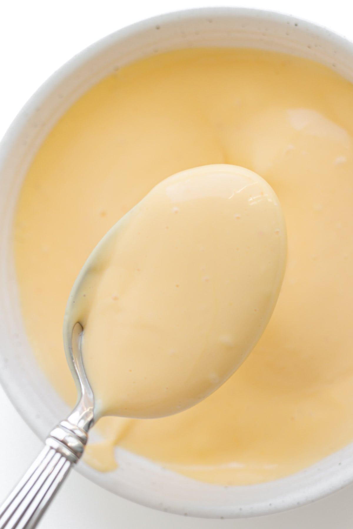 Spoonful of hollandaise sauce lifted over bowl.