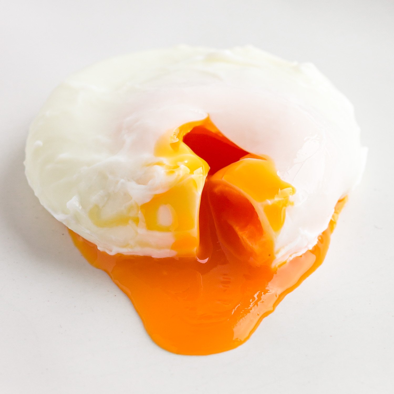 Closeup of a poached egg that has been cut into to release the golden, runny yolk.