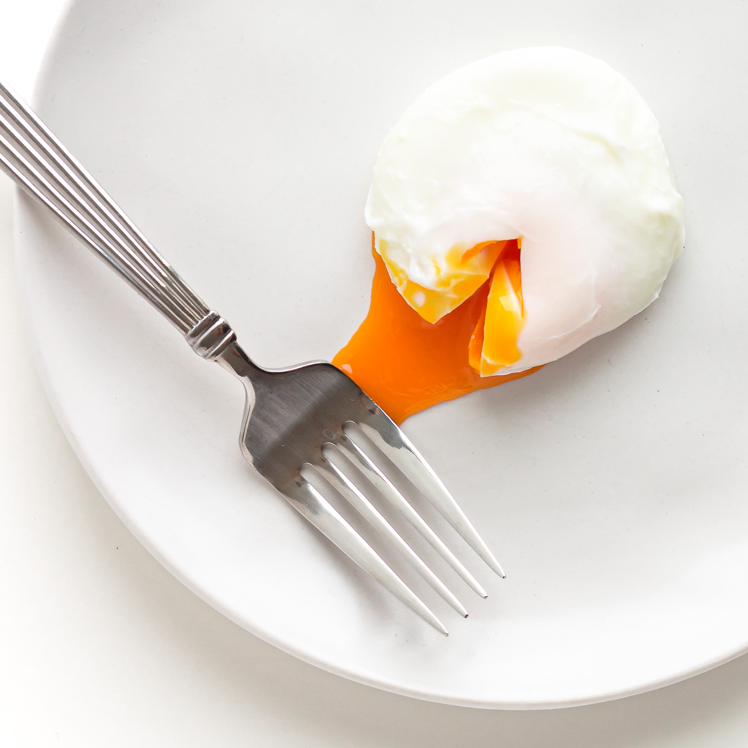A single poached egg with some yolk oozing out on a white plate with a fork.