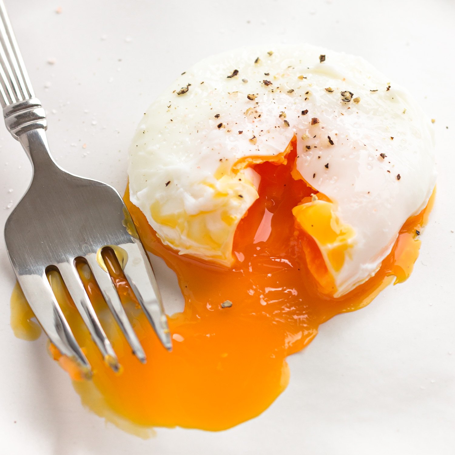 A seasoned poached egg next to a fork with the golden, oozy yolk running out.