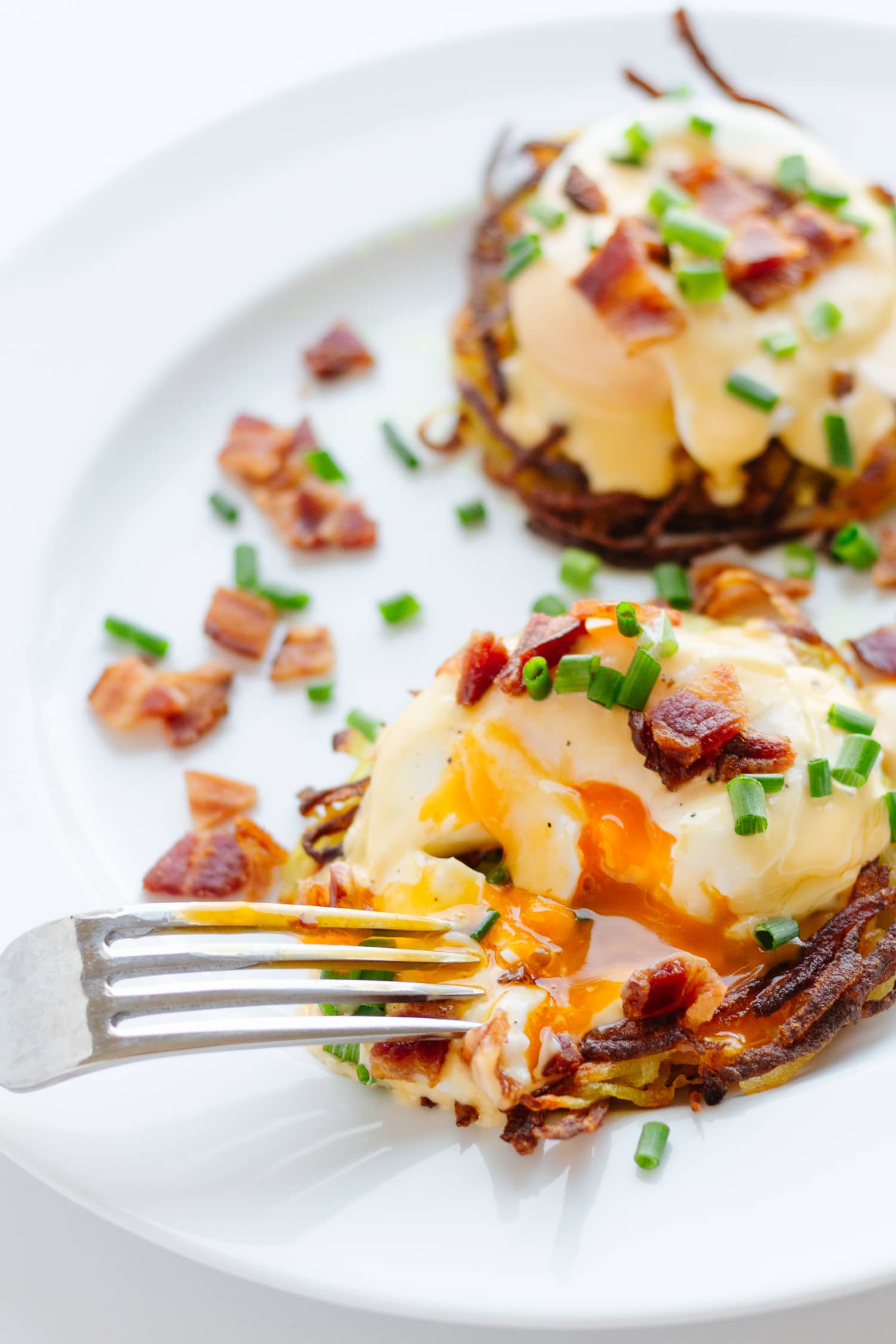 Two rosti eggs benny on a white plate with a fork cutting into one of them.