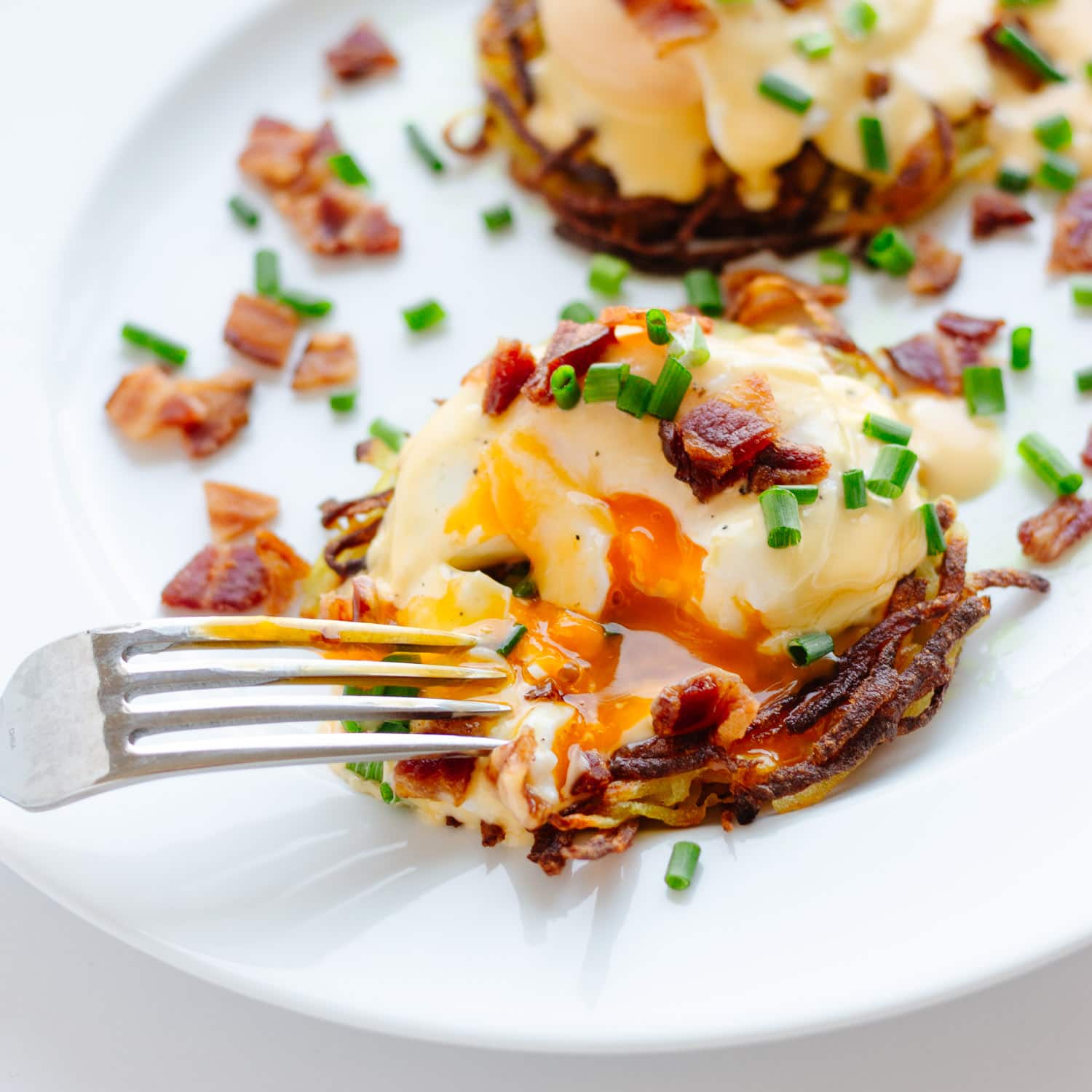 Rosti Eggs Benny on a white plate with fork digging in.