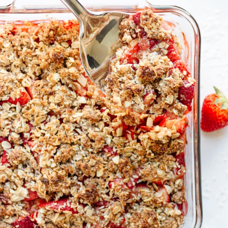 Serving spoon digging into a square glass dish of Strawberry Coconut Crisp.