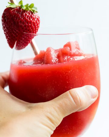 Hand holding glass of strawberry wine slushie.