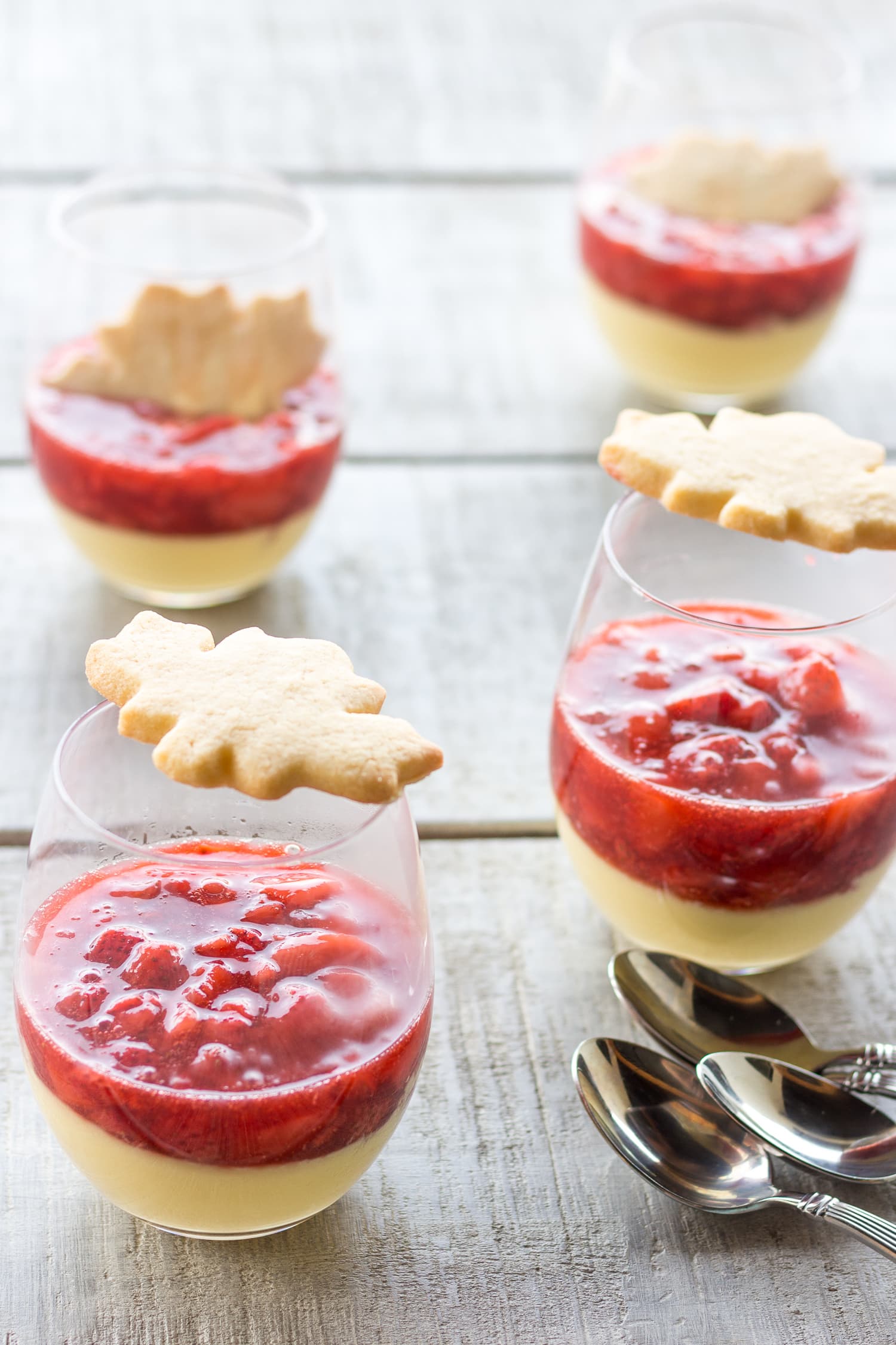 4 glasses of maple custard with strawberry compote topped with a maple leaf shaped sugar cookie