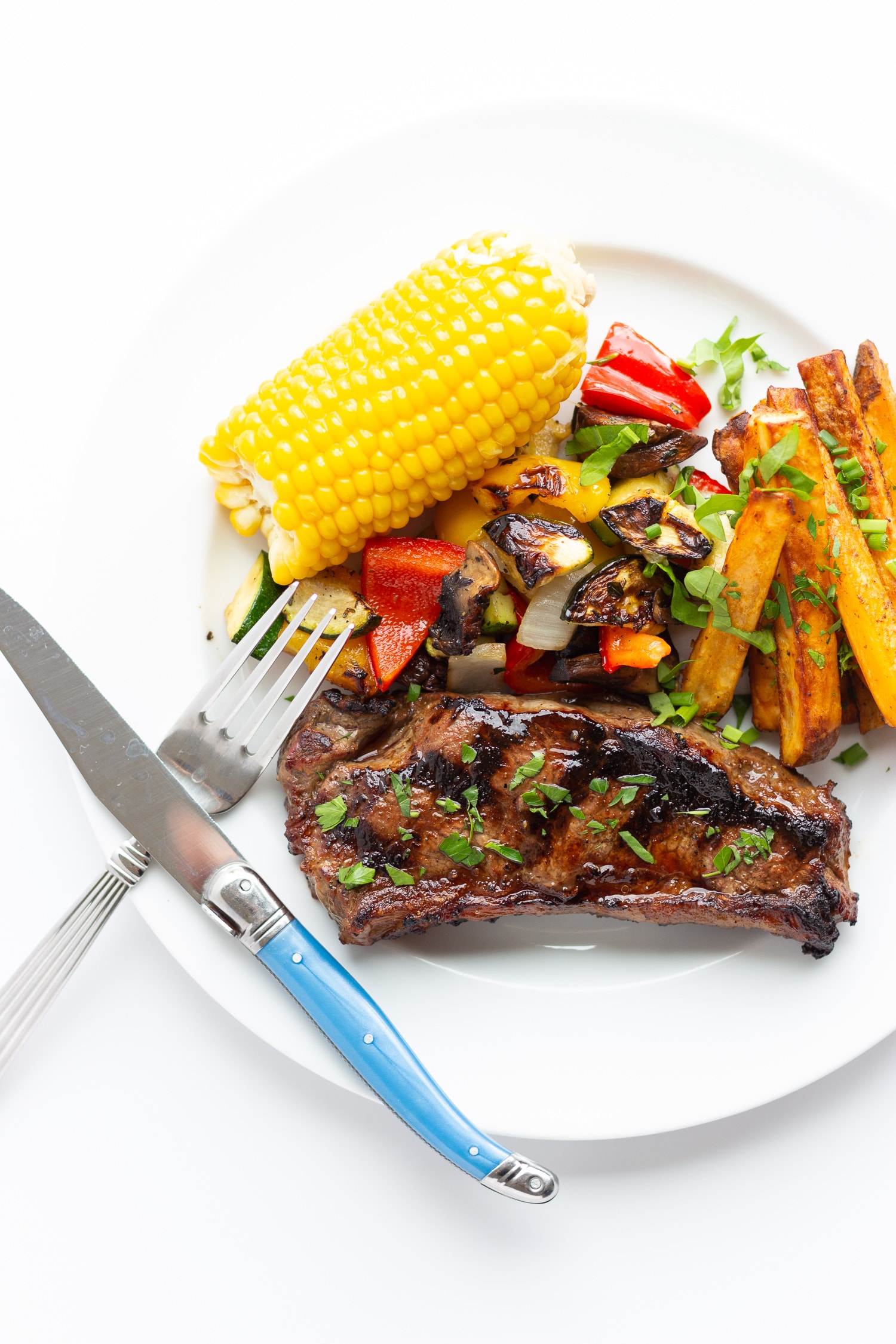 Grilled steak dinner on a white plate with fork and knife crossed in the corner