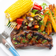 Grilled steak dinner on a white plate with fork and knife.