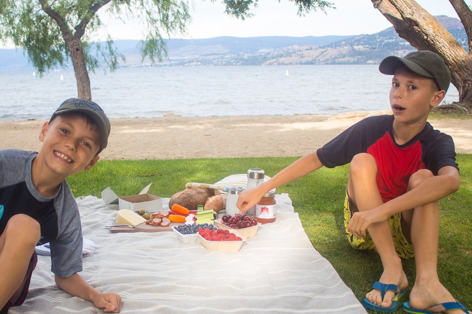 Two boys sitting next to a picnic by the beach