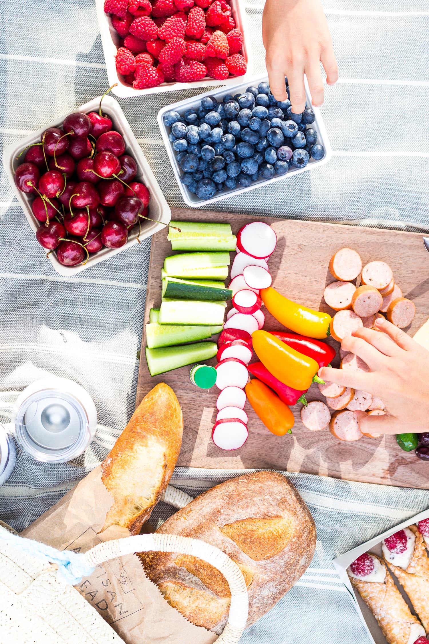 Overhead shot of picnic food on a blanket with two hands reaching in