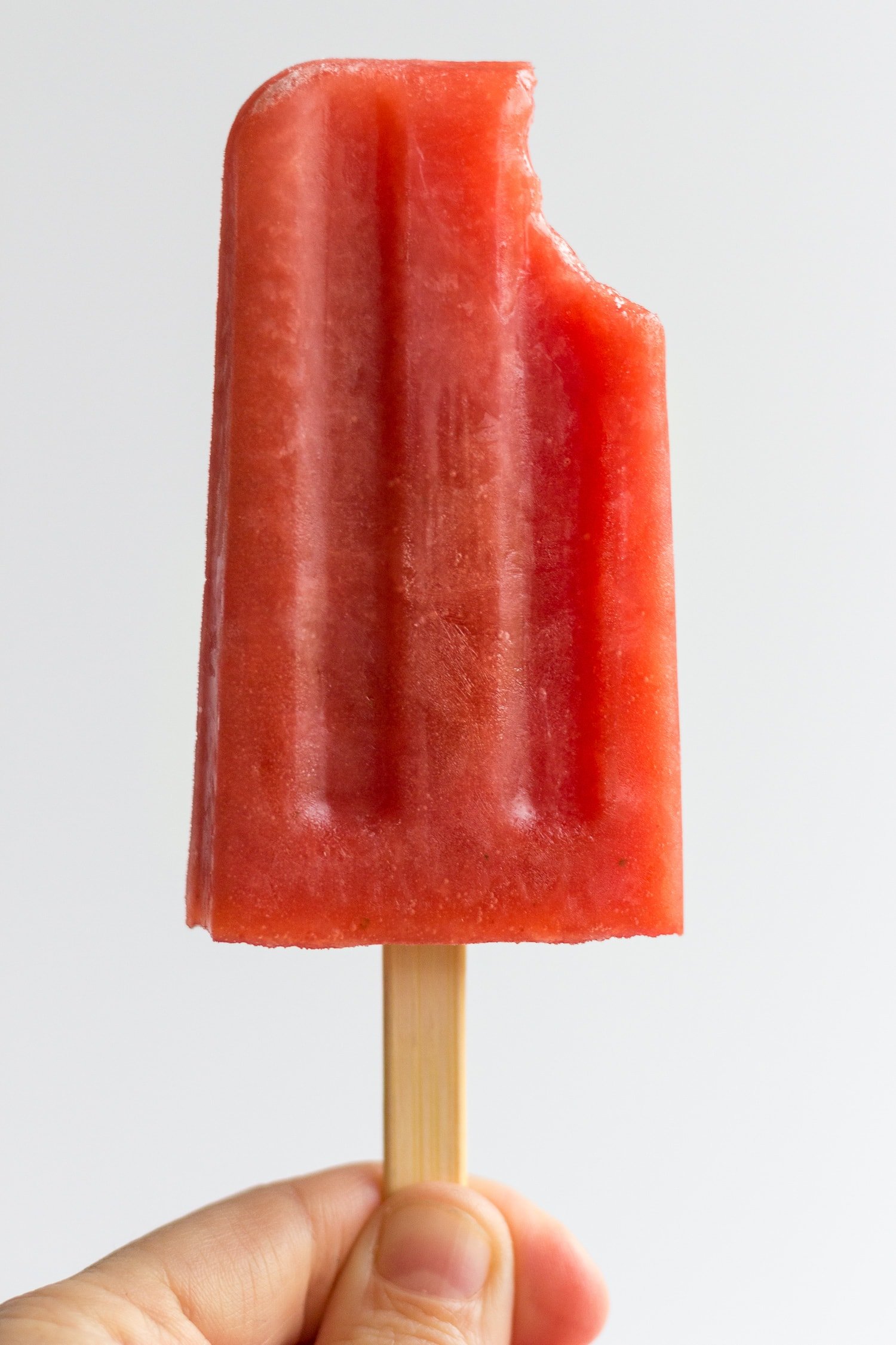 Hand holding a watermelon strawberry popsicle with a bite taken out of it