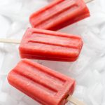 Four watermelon strawberry popsicles sitting on a bed of ice.