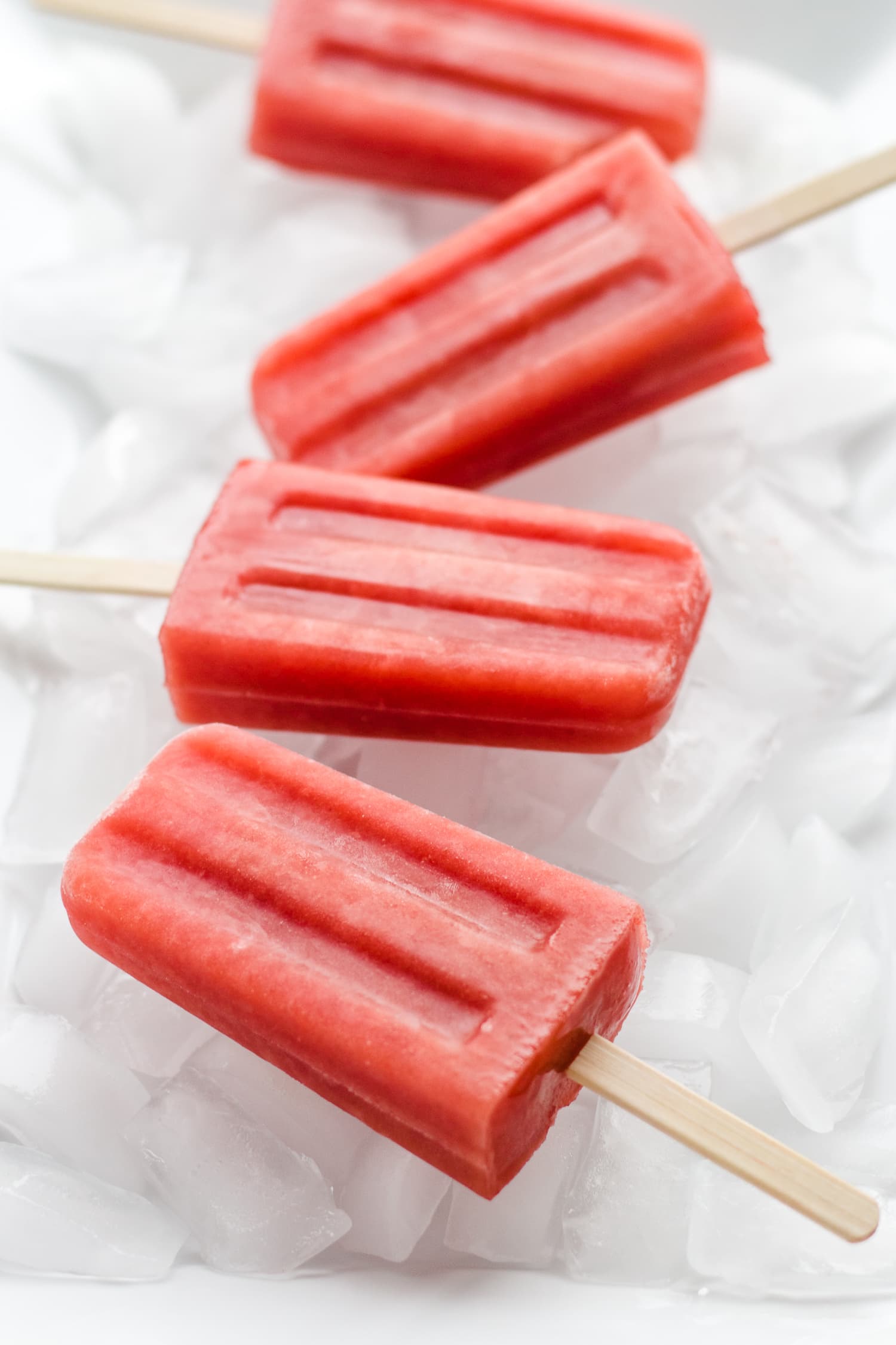 Four watermelon strawberry popsicles sitting on a bed of ice.