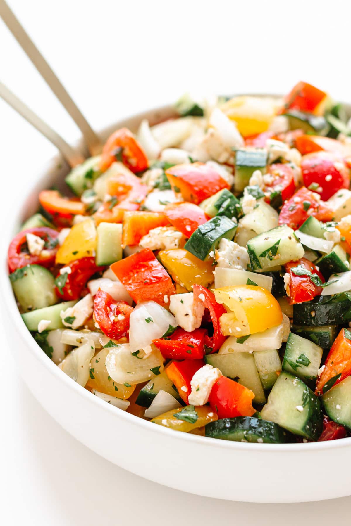 White bowl of chopped salad with gold salad servers sticking out.