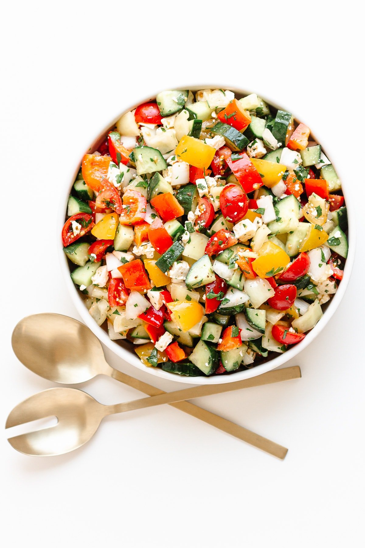 Bowl of summer chopped salad and gold salad servers on a white background.