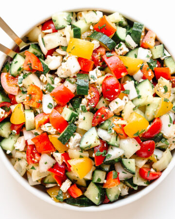 Bowl of chopped veggie salad with gold colored salad servers sticking out.