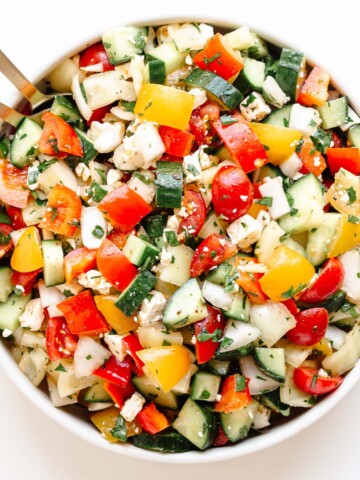 Bowl of chopped veggie salad with gold colored salad servers sticking out.