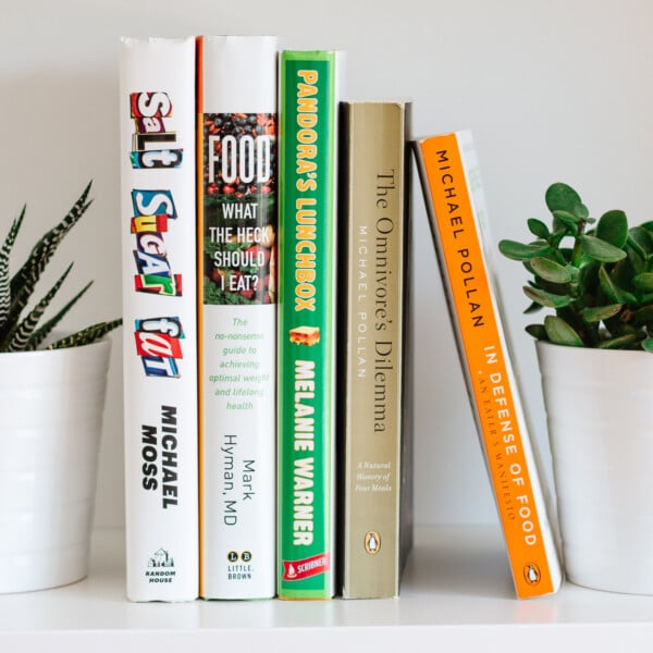 Five books on a white shelf with plants on each end.