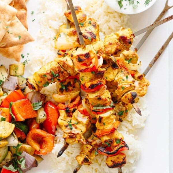 Grilled Tandoori Chicken Kebabs piled on some rice and surrounded by other sides.