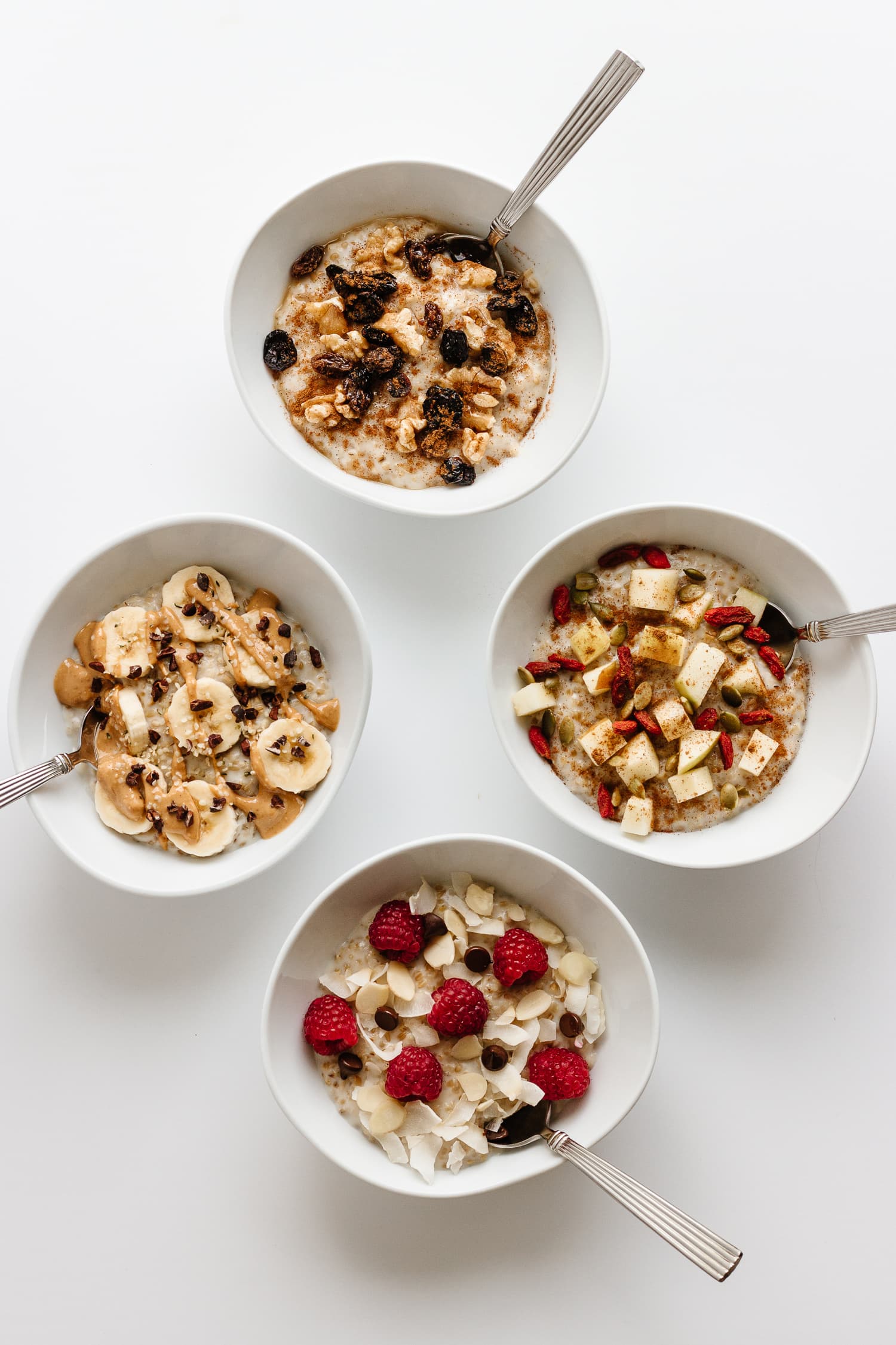 Four white bowls of steel cut oats with various toppings on a white background