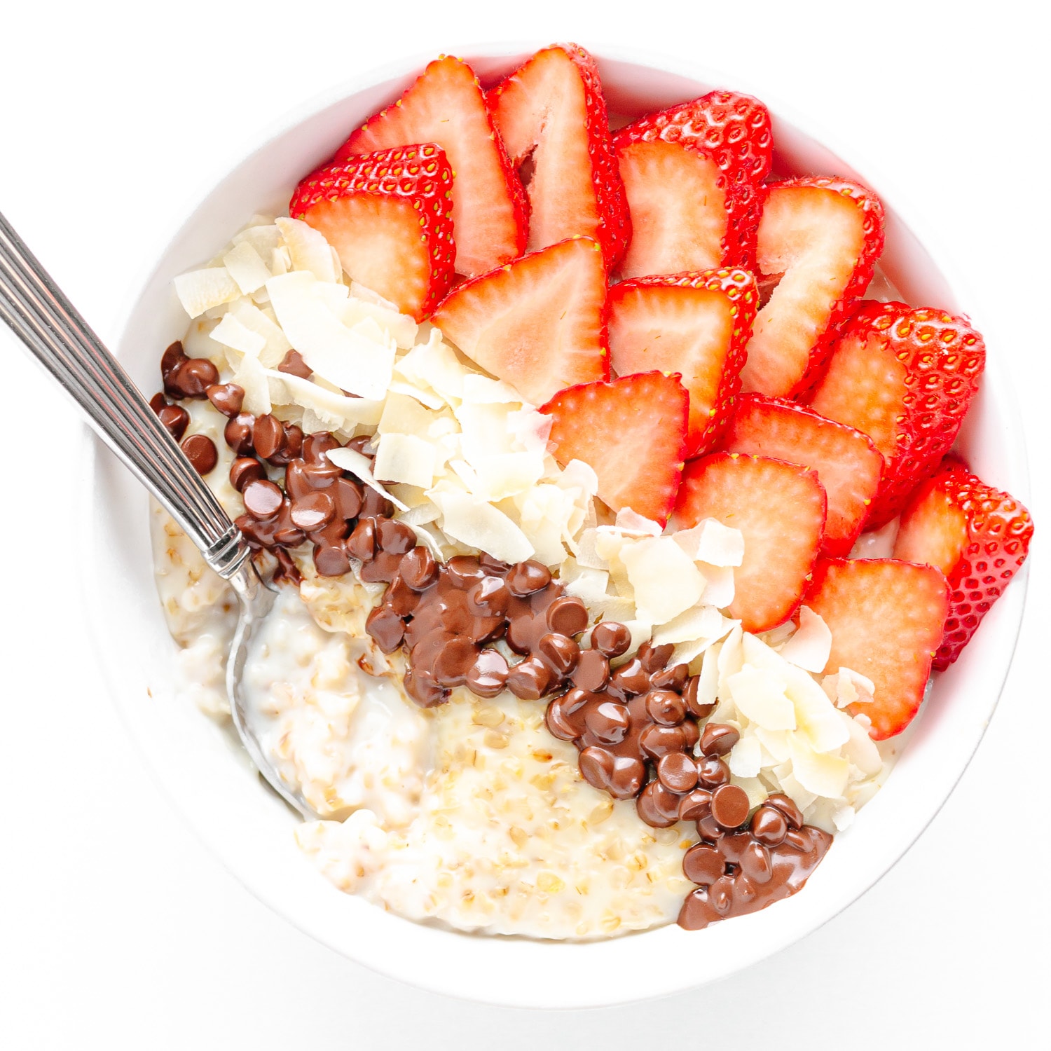 Bowl of creamy steel cut oats topped with sliced strawberries, coconut flakes and mini chocolate chips.