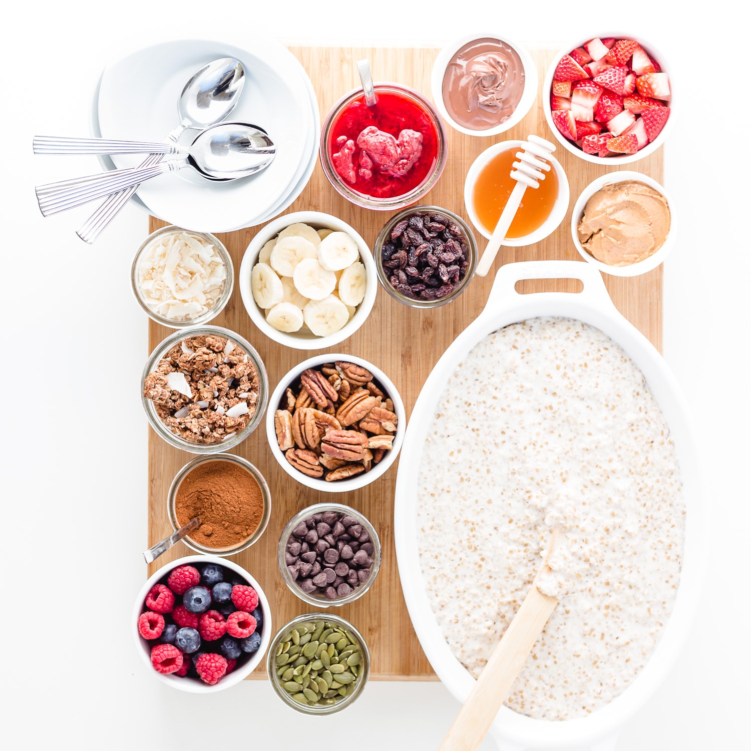 An oatmeal breakfast board featuring a variety of toppings set out in little bowls on a board alongside a big dish of oatmeal.