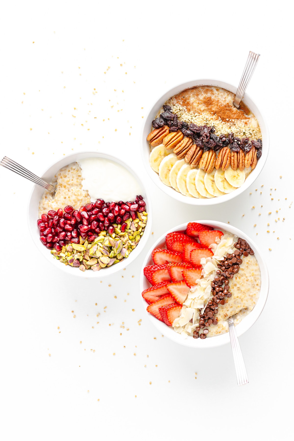 Three bowls of steel cut oatmeal with different toppings on a white background scattered with steel cut oats.