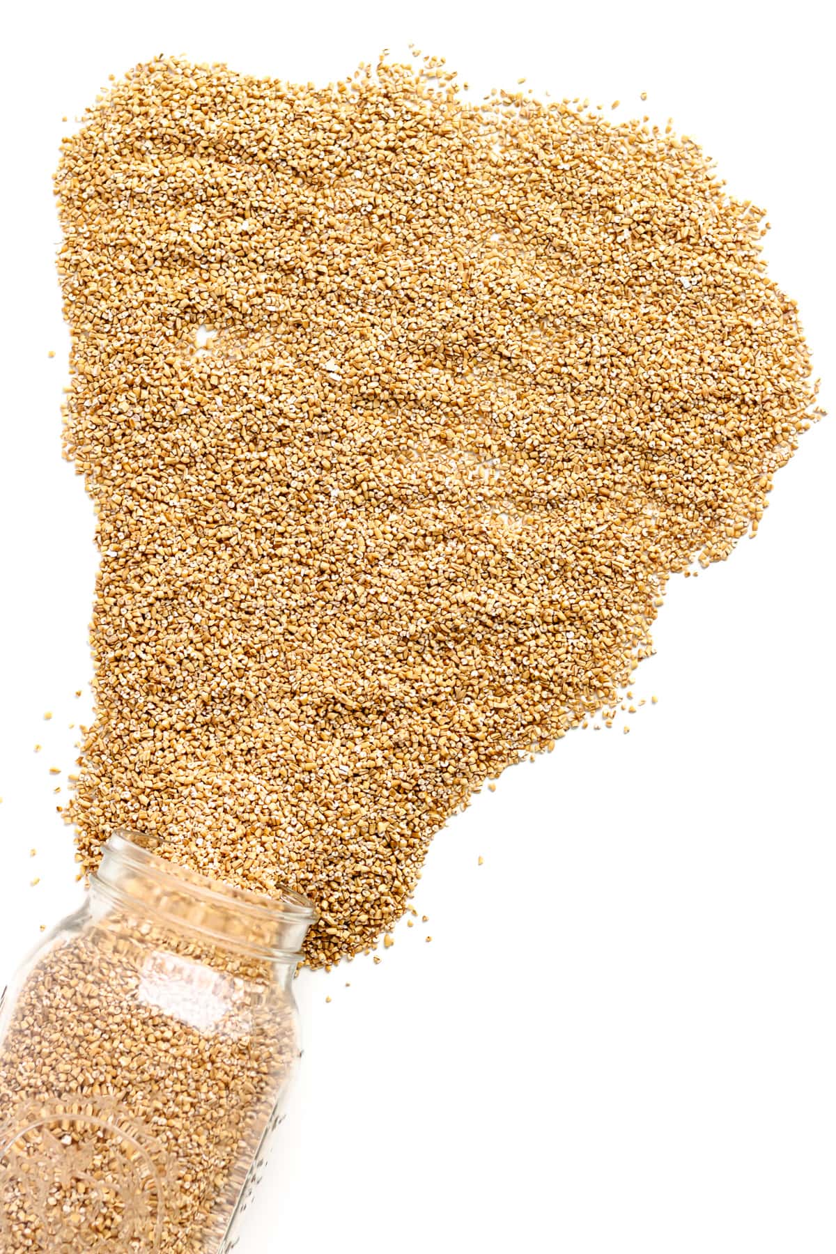 Steel cut oats spilling out of a glass mason jar across a white background.