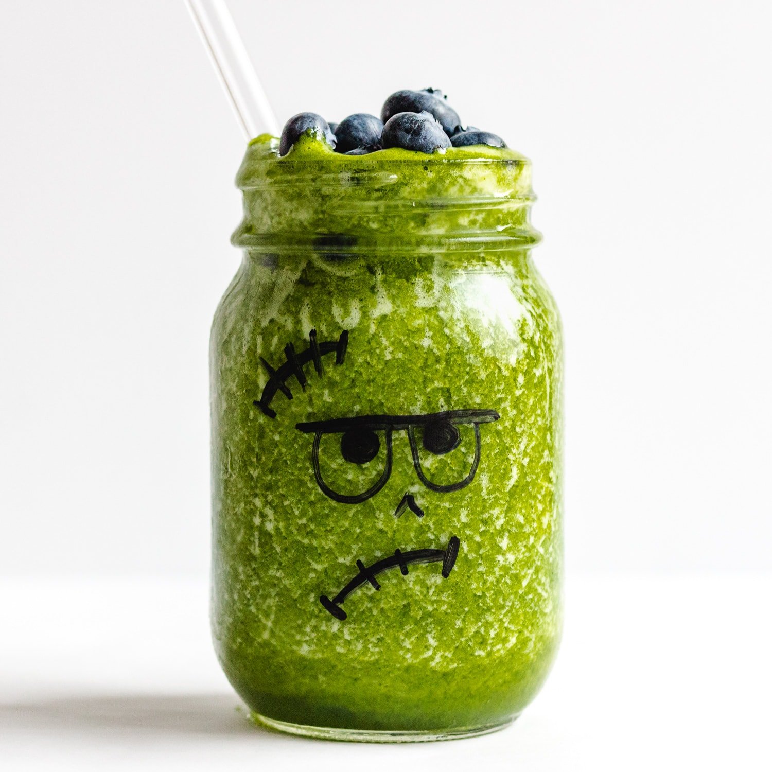 A green smoothie poured into a jar that has a Frankenstein face drawn on and topped with blueberries.