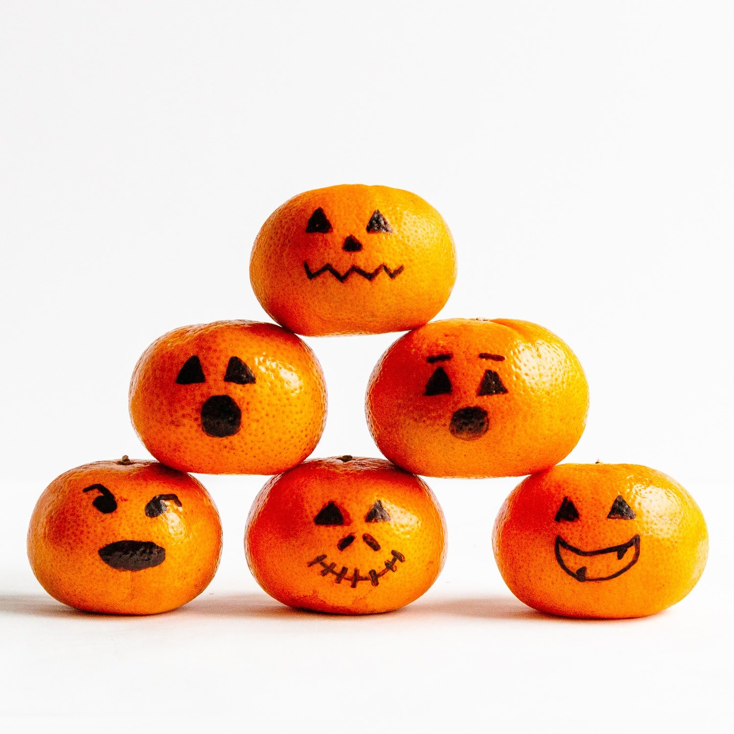 A pyramid of mandarins with faces drawn on with black permanent marker to look like Jack O' Lanterns.