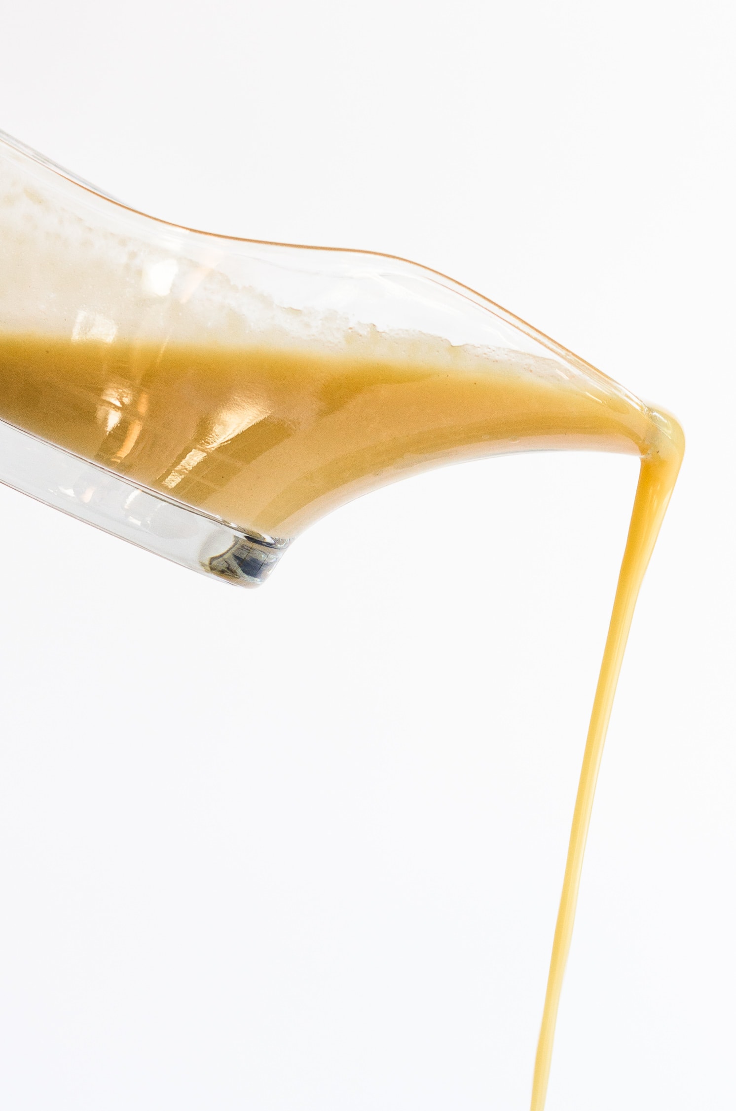 Turkey Gravy pouring down from a clear glass gravy server on a white background.