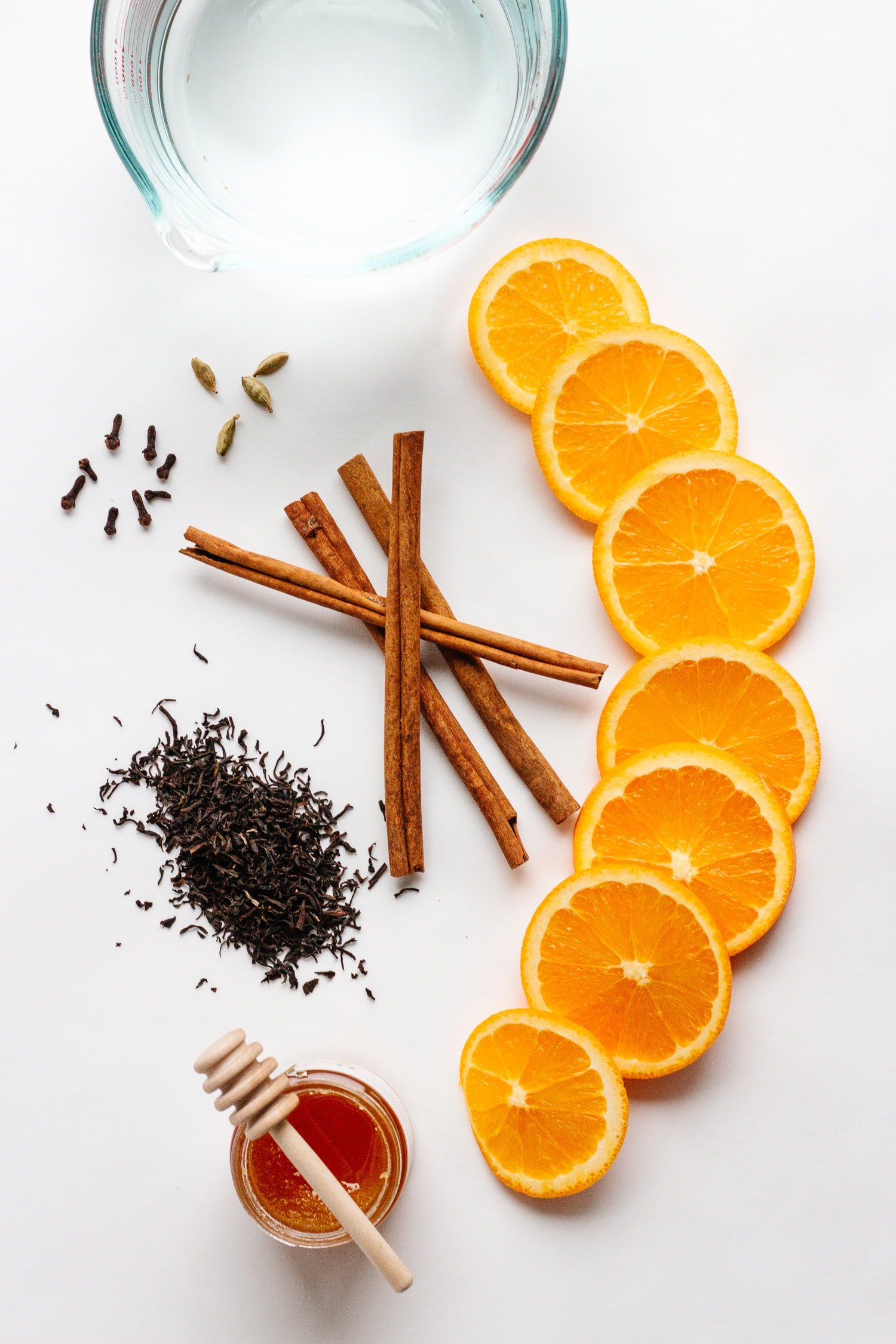 Overhead shot of ingredients for Orange Spice Mulled Tea: water, loose leaf black tea, orange slices, cinnamon sticks, cardamom pods, cloves