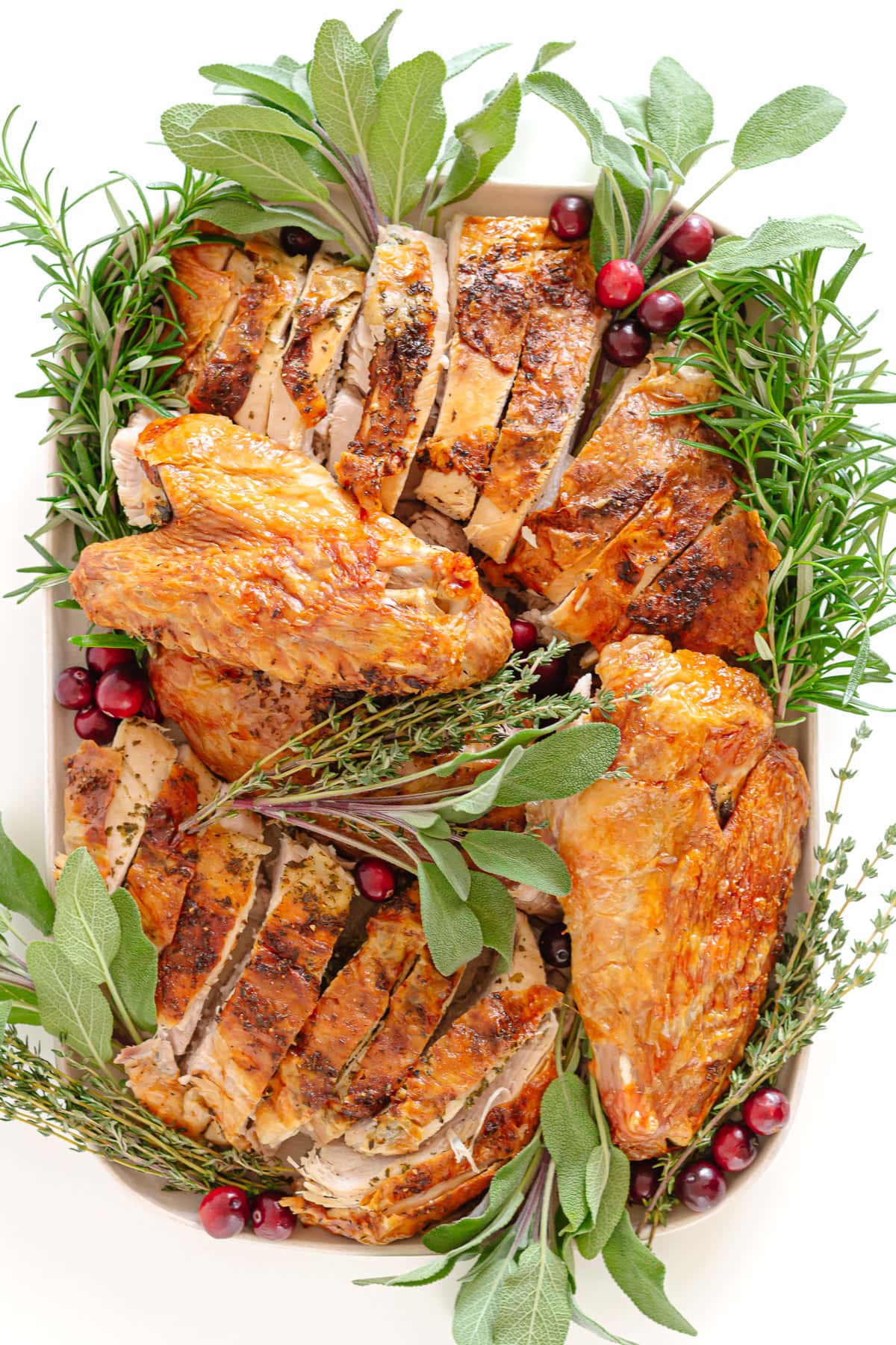 Platter of carved roast turkey garnished with herbs and fresh cranberries.